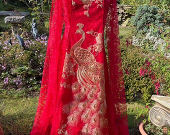 Puede incluir: Un vestido largo de encaje rojo con un diseño de pavo real dorado. El vestido tiene mangas largas y un escote cuadrado.