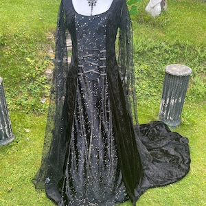 May include: A black velvet gown with a lace overlay and a gold glitter design. The gown has a fitted bodice and a flowing skirt with a train.