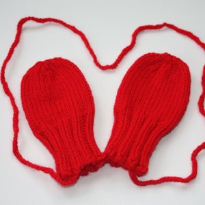 May include: Red knitted baby mittens with a matching string tie.