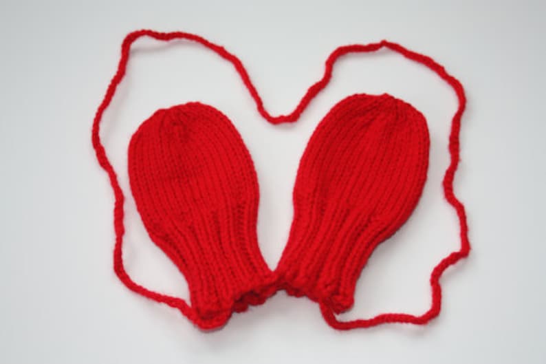 May include: Red knitted baby mittens with a matching string tie.