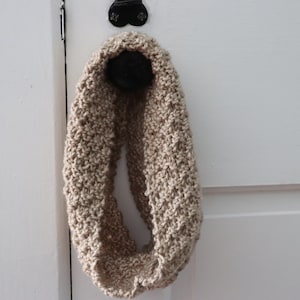 beige knitted seed stitch cowl scarf hanging from a doorknob