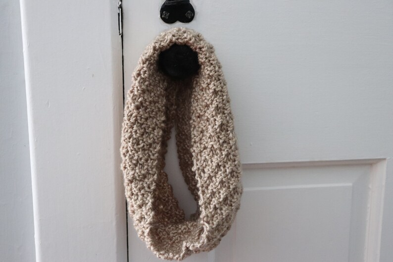beige knitted seed stitch cowl scarf hanging from a doorknob