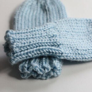 May include: A pair of light blue knitted mittens with a ribbed cuff. The mittens are folded together and the cuff is turned up.