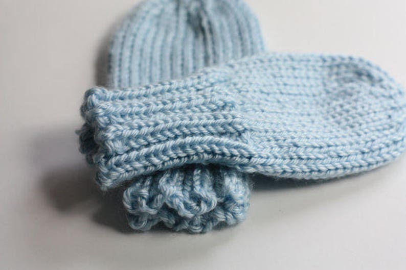May include: A pair of light blue knitted mittens with a ribbed cuff. The mittens are folded together and the cuff is turned up.