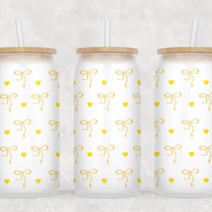 May include: Three white stainless steel tumblers with yellow bows and hearts patterns. Each tumbler has a bamboo lid and a clear plastic straw.