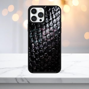 May include: A black smartphone case featuring a textured, dark, hexagonal scale pattern across the back. The case has a black frame and a cutout for a triple-lens camera system. Two faint, circular, outline-style icons are visible on the surface.