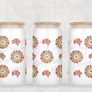 May include: Three white glass tumblers with bamboo lids and straws. Each tumbler is decorated with a repeating pattern of brown and orange sun-like designs and Australian continent shapes. The text "Emma Mae Designs" is visible on the tumblers.