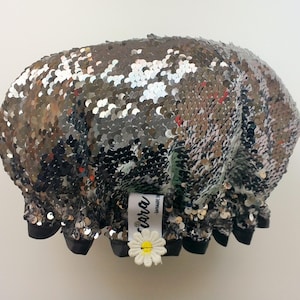 May include: A silver and black shower cap with sequins. The cap has a black elastic band and a white tag that says "cora" handmade.