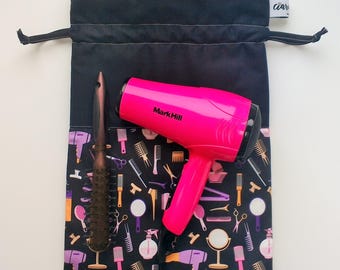 Puede incluir: Una bolsa de cordón negro con un secador de pelo rosa y un cepillo de pelo marrón. La bolsa tiene un patrón blanco y negro de herramientas para peinar el cabello.