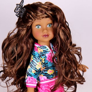 May include: A doll with long brown curly hair, wearing a blue and pink patterned jacket and a pink skirt. She has green eyes and brown skin.
