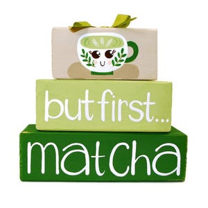 May include: A three-tiered wooden block set with a matcha theme. The top block features a cute matcha cup illustration. The middle block says "but first..." and the bottom block says "matcha" in white script.