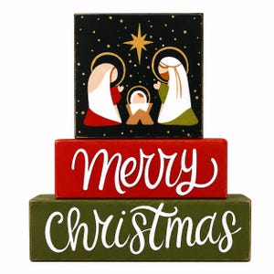 May include: A stack of three rectangular wooden blocks. The top block is black with a gold star and a nativity scene. The middle red block features the white text "merry" in script. The bottom green block features the white text "Christmas".