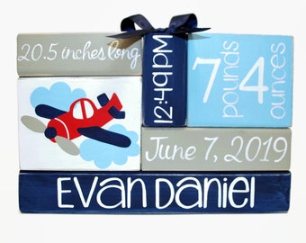 May include: A set of five wooden blocks with a blue, red, and white airplane design. The blocks are stacked and display the text "Evan Daniel", "June 7, 2019", "7 pounds 4 ounces", "12:21", and "20.5 inches long".