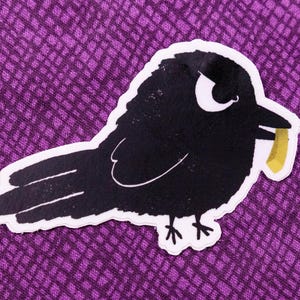 May include: A black crow with a yellow stick in its beak. The crow has a white eye and is looking to the right.