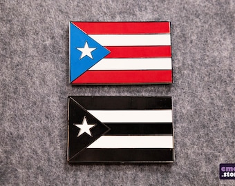May include: Two enamel pins featuring the flag of Puerto Rico. The top pin is the traditional red, white, and blue flag. The bottom pin is a black and white version of the flag.