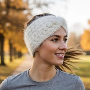 May include: A wide, off-white knitted headband featuring a fuzzy, textured yarn construction with a central twisted knot detail. The accessory is crafted from a soft, thick material that covers the ears and forehead, providing a warm, layered look.
