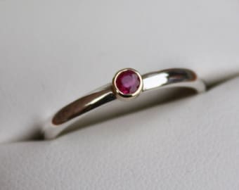 May include: A simple silver band ring with a single red ruby gemstone set in a gold bezel.