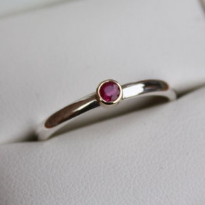 May include: A simple silver band ring with a single red ruby gemstone set in a gold bezel.