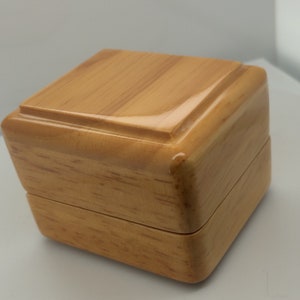 May include: A small, wooden box with a light brown finish. The box has a hinged lid and a smooth, polished surface.