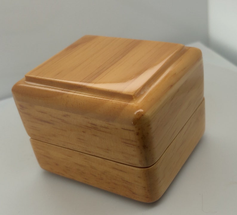 May include: A small, wooden box with a light brown finish. The box has a hinged lid and a smooth, polished surface.