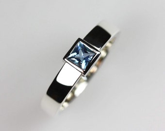 May include: A silver ring with a square blue gemstone set in a silver band.