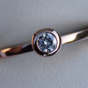 May include: A rose gold ring with a bezel setting featuring a round, clear diamond.
