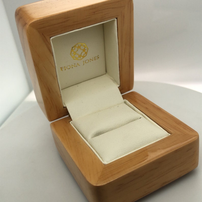 May include: A wooden ring box with a white interior and the text "Fiona Jones" on the lid.
