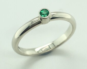 May include: A simple silver band ring with a single, small, round, green emerald gemstone.