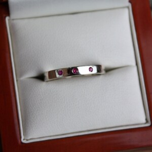 May include: A silver band ring with three small pink gemstones set into the band.