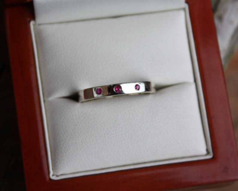 May include: A silver band ring with three small pink gemstones set into the band.