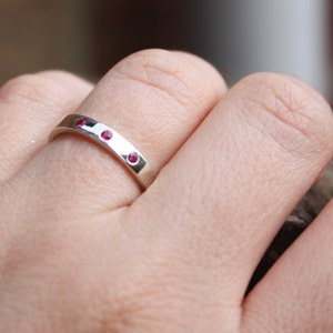 May include: A silver band ring with three small red gemstones set into the band.