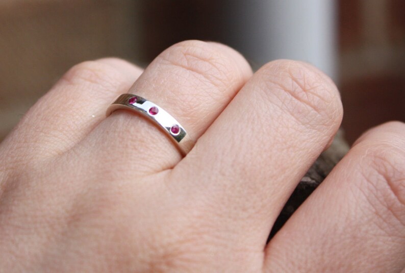 May include: A silver band ring with three small red gemstones set into the band.