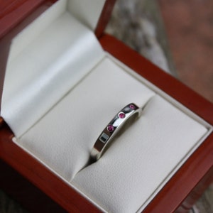 May include: A silver band ring with five small pink gemstones set into the band.