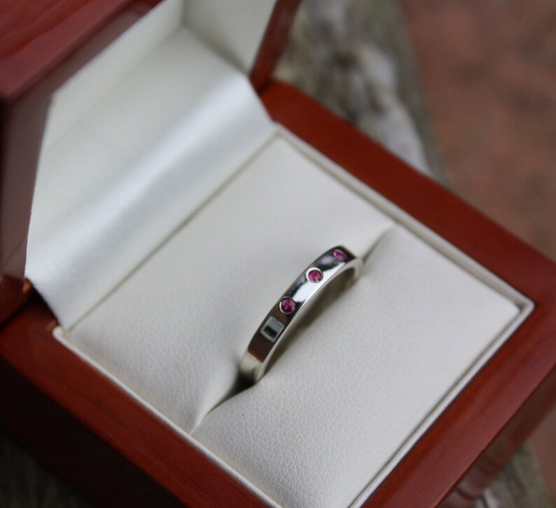 May include: A silver band ring with five small pink gemstones set into the band.