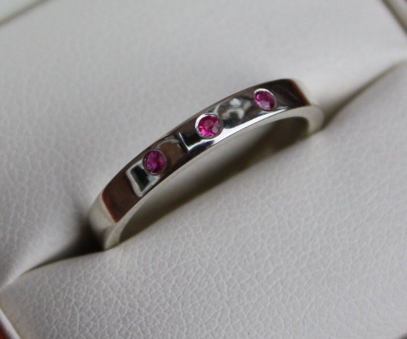May include: A silver band ring with three small pink gemstones set in the band.