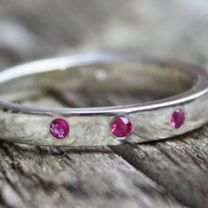 May include: A silver band ring with three small pink gemstones set into the band.