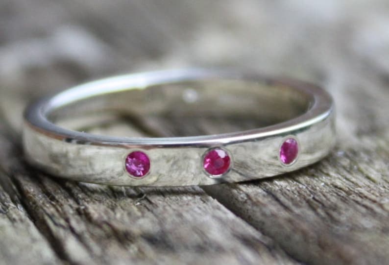 May include: A silver band ring with three small pink gemstones set into the band.