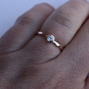 May include: A simple rose gold band ring with a single, clear round gemstone.