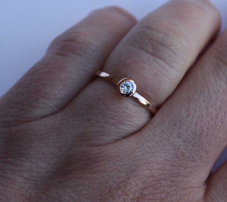 May include: A simple rose gold band ring with a single, clear round gemstone.