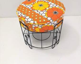 May include: A round black metal stool with a floral patterned cushion. The cushion has orange and yellow flowers on a white background.