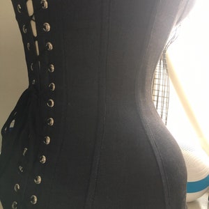 May include: A black corset with a lace-up back and metal eyelets. The corset is made of a smooth, stretchy fabric and has a fitted silhouette.