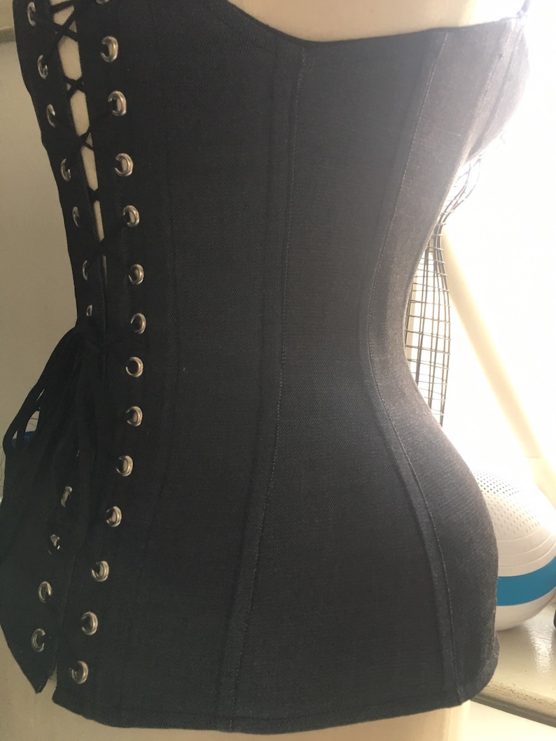 May include: A black corset with a lace-up back and metal eyelets. The corset is made of a smooth, stretchy fabric and has a fitted silhouette.