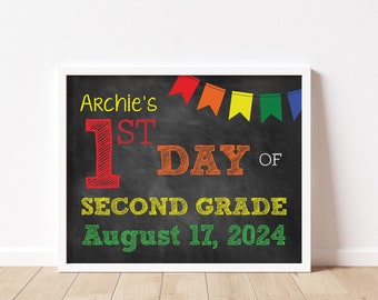 Może przedstawiać: Tablica z napisem "Archie's 1st Day of Second Grade August 17, 2024". Tablica jest ozdobiona tęczową girlandą.