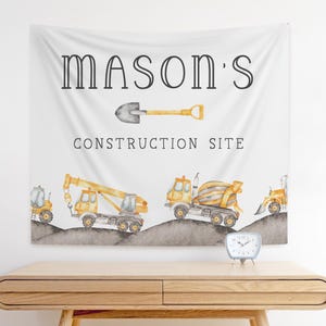 Op de afbeelding: Een witte banner met de tekst "Mason's Construction Site" in zwarte letters. De banner toont een gele schop, een gele betonmixer, een gele kraan en een gele bulldozer.