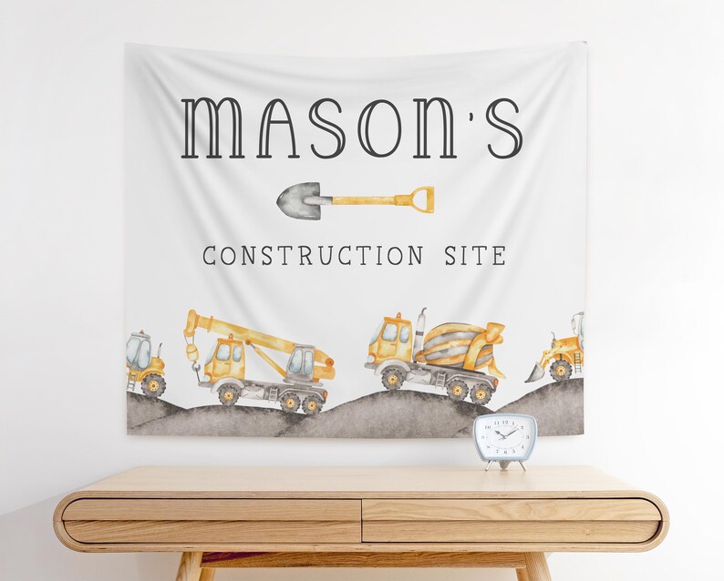 Op de afbeelding: Een witte banner met de tekst "Mason's Construction Site" in zwarte letters. De banner toont een gele schop, een gele betonmixer, een gele kraan en een gele bulldozer.