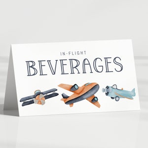 May include: A white folded card with the text IN-FLIGHT BEVERAGES printed in dark blue. Below the text are three watercolor illustrations of airplanes: a dark blue biplane, an orange monoplane, and a light blue propeller airplane.