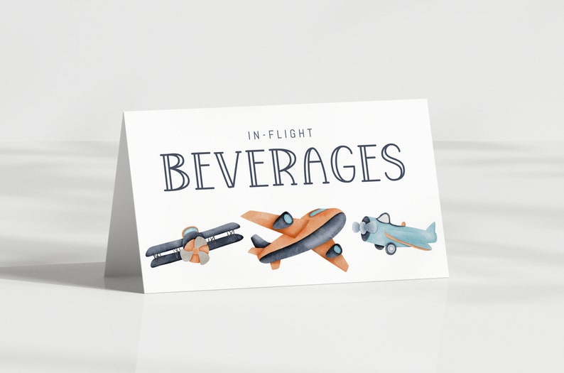 May include: A white folded card with the text IN-FLIGHT BEVERAGES printed in dark blue. Below the text are three watercolor illustrations of airplanes: a dark blue biplane, an orange monoplane, and a light blue propeller airplane.