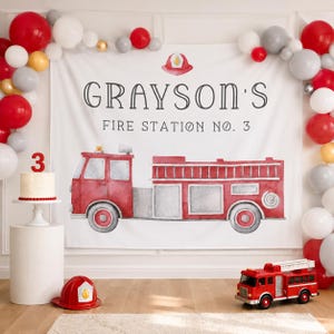 May include: A white backdrop featuring a watercolour red fire engine, a red fire helmet icon, and the text "GRAYSON'S FIRE STATION NO. 3". The scene includes a balloon arch in red, white, and grey, a white cake with a red number 3 topper, and a toy fire engine.