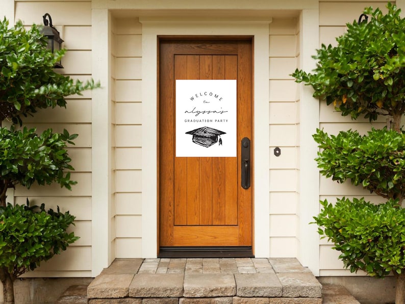 Pu&ograve; includere: Una porta di legno con un cartello bianco che recita "Welcome to Alyssa's Graduation Party" in corsivo nero. Un'illustrazione in bianco e nero di un cappello di laurea &egrave; sotto il testo. La porta &egrave; incorniciata da rivestimenti bianchi e cespugli verdi.