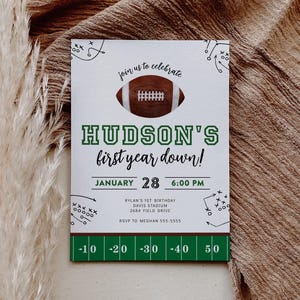 Könnte beinhalten: Eine rechteckige Einladung mit Football-Motiv. Die Einladung zeigt eine Football-Grafik und den Text "Hudson's first year down!" in Grün. Zusätzlicher Text enthält Datum, Uhrzeit und RSVP-Informationen.
